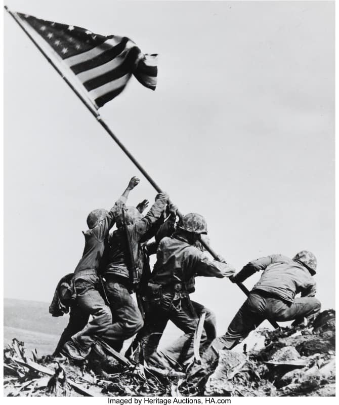 Marines raise a U.S. flag on a rubble-covered hill amid battle debris in WWII iconic scene.