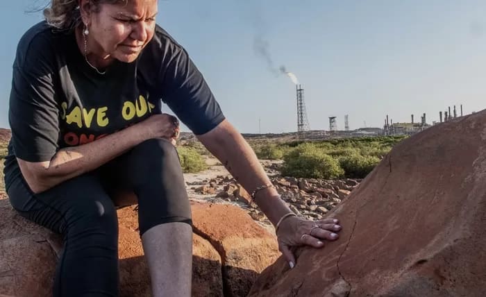 Raelene Cooper and an ancient Turtle Petroglyph with a flaring gas facility behind them