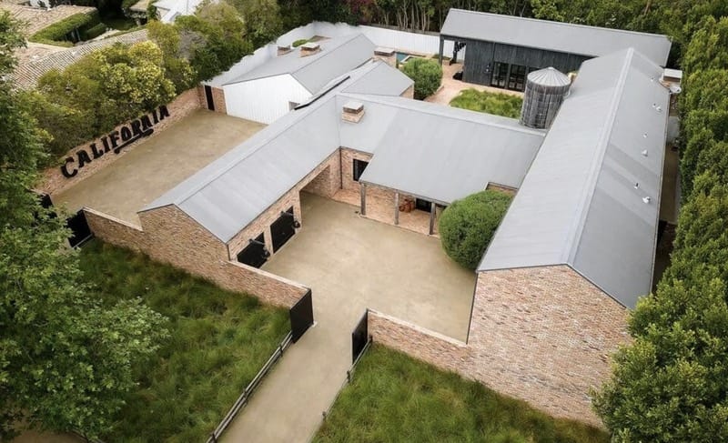Diane Keaton Home - 1EarthMedia Aerial view of a brick building complex with gray metal roofs, a central courtyard, and a large 'CALIFORNIA' sign on a brick wall surrounded by greenery.