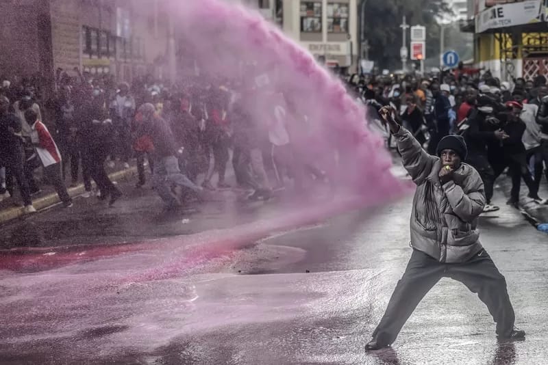 009_Africa_Stories_Luis Tato_Agence France-Presse - 1EarthMedia “Marked by Defiance” © Luis Tato, Agence France-Presse — used with permission World Press Photo A young protester, drenched in pink-dyed water from a police water cannon, raises his fist in defiance. The dye, often used to mark demonstrators for later arrest, becomes a badge of resistance in this 20 June 2024 scene. The symbolism is potent—these youth will not be washed away.