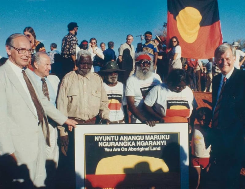 UluruHandback02 - 1EarthMedia Traditional owners Peter Bulla, Peter Kanari, Nipper Winmarti and his wife, Barbara Tjirkadu, with Sir Ninian Stephen and Clyde Holding (left) and Barry Cohen (right), 26 October 1985. Image: National Museum of Australia