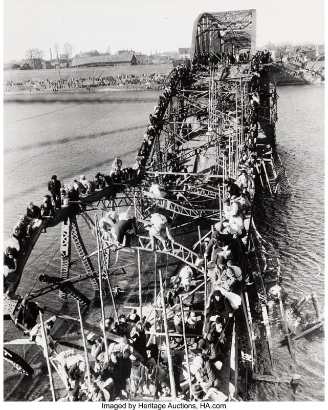 Max Desfor - 1EarthMedia Crowd on a large metal truss bridge spanning a river, with many people lining the structure toward the far bank.